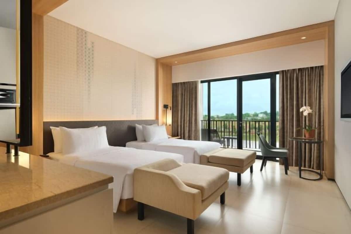 Een hotelkamer met twee bedden, een kleine zithoek, een bureau en een balkon met uitzicht.