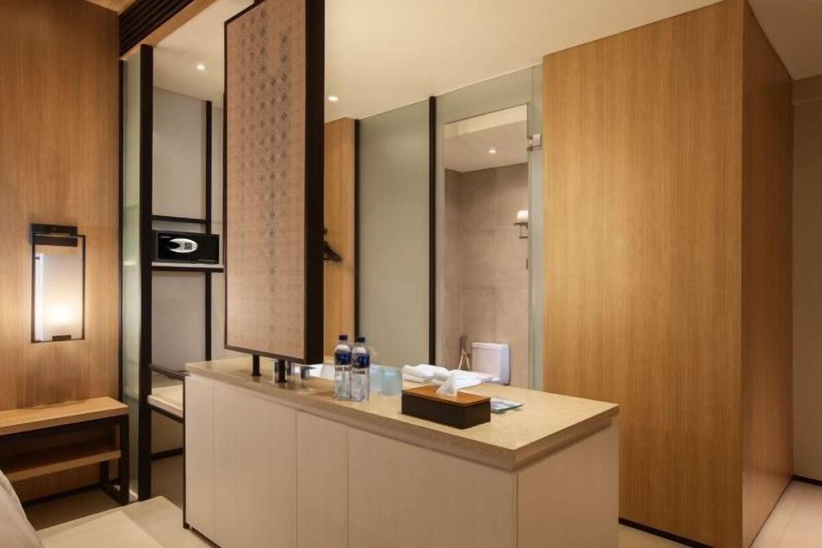 A modern bathroom with a wooden vanity, a large mirror, and a towel dispenser.