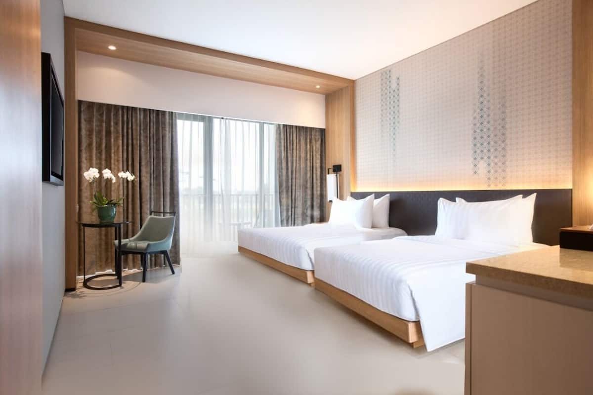 Een moderne hotelkamer met twee bedden, een bureau, een stoel en een groot raam met gordijnen.