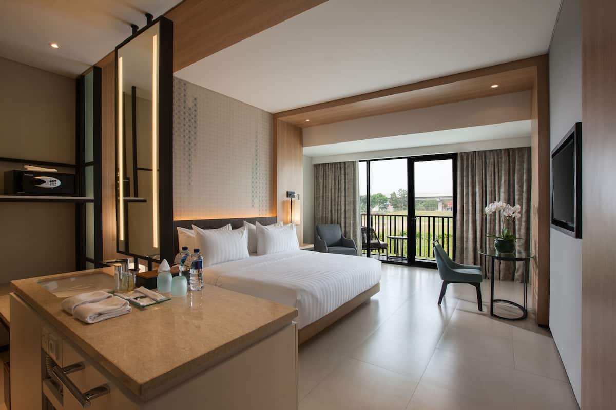 Een moderne hotelkamer met een groot bed, een bureau met spiegel, een stoel en een balkon met uitzicht.