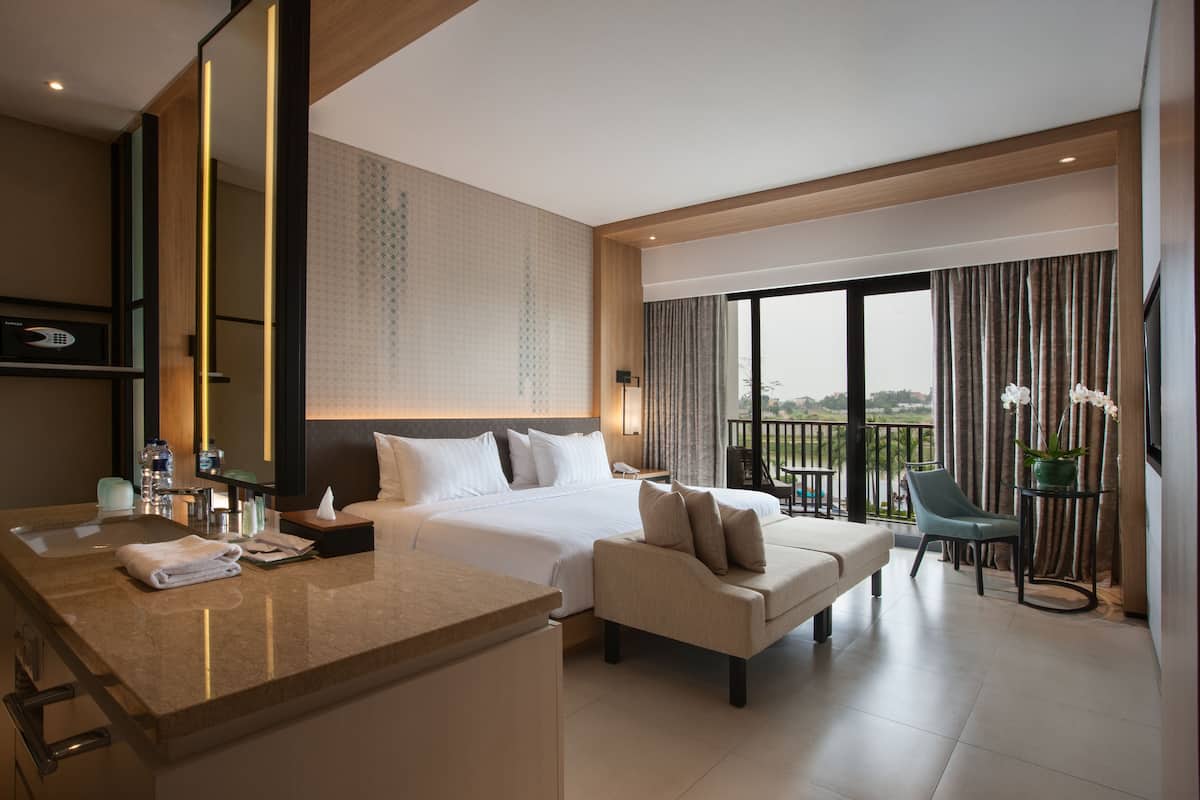Een moderne hotelkamer met een groot bed, een zithoek, een balkon met uitzicht en een badkamer met een grote spiegel en wastafel.