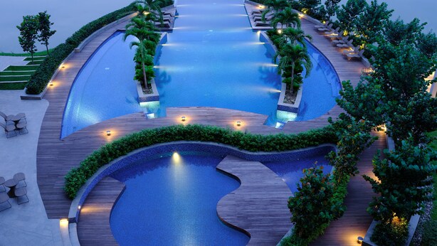 Une grande piscine à plusieurs niveaux, dotée de gradins et entourée de verdure.