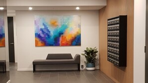 Eine moderne Lobby mit einem grauen Sofa, einem großen abstrakten Gemälde, einem Blumentopf und einem an der Wand befestigten Schrank.