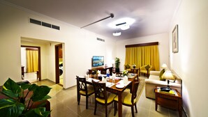 A well-lit living room with a dining area, a sofa, and a TV on the wall. - Rose Garden Hotel Apartments - Bur Dubai (Dubai)