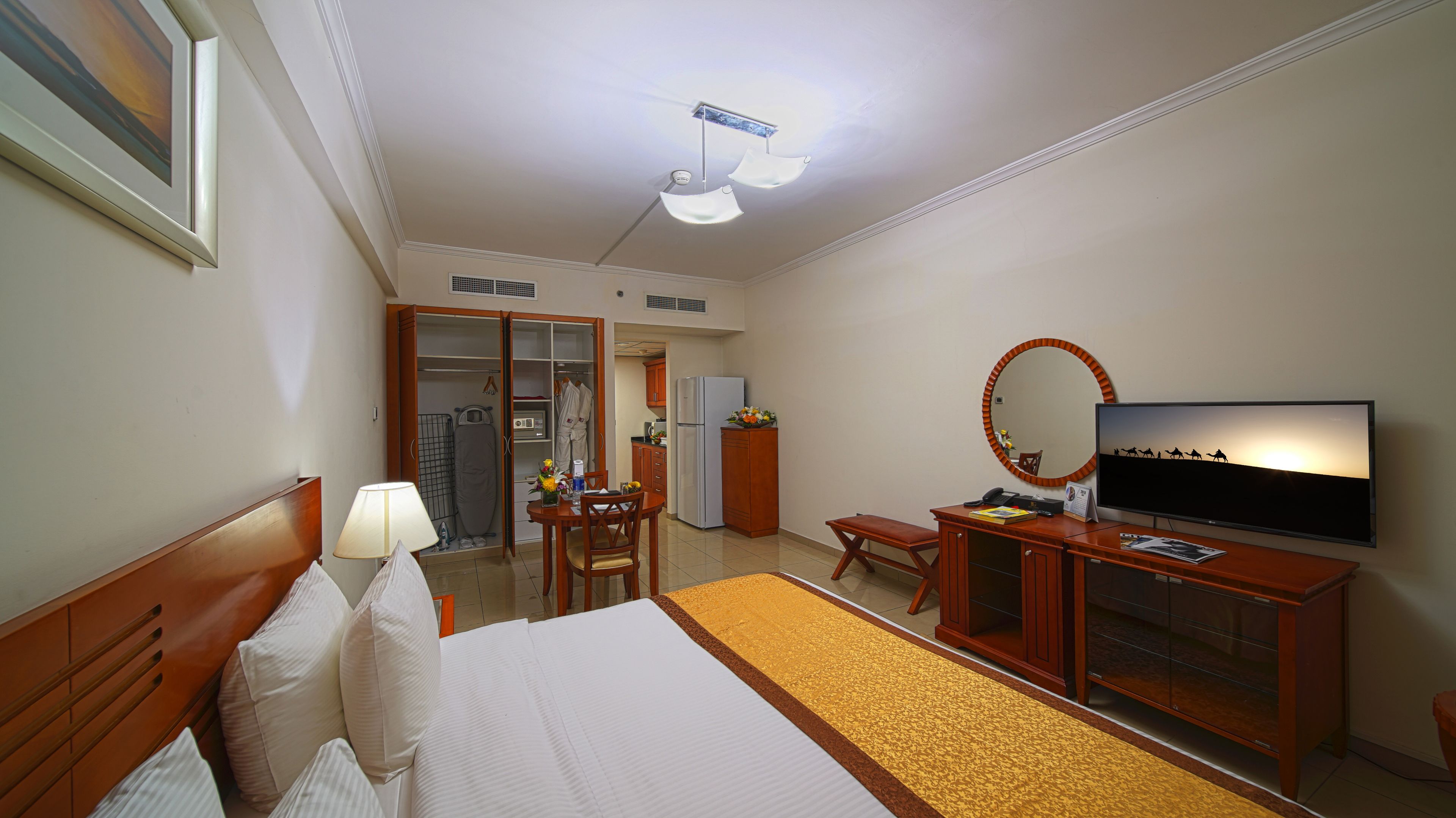 A hotel room with a bed, a desk with a TV, a wardrobe, and a bathroom visible through an open door.