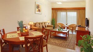 A well-lit living room with a sofa, a dining table with chairs, a coffee table, and a TV. - Rose Garden Hotel Apartments - Bur Dubai (Dubai)