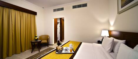 Quarto de hotel com uma cama, uma cadeira, uma mesinha com uma bandeja de itens de café da manhã e uma porta que dá para um banheiro.