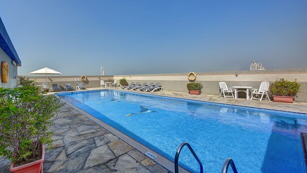 A swimming pool with lounge chairs and potted plants, a clear sky, and a distant building. - Rose Garden Hotel Apartments - Bur Dubai (Dubai)