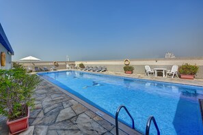 A swimming pool with lounge chairs and potted plants, a clear sky, and a distant building. - Rose Garden Hotel Apartments Bur Dubai (Dubai)