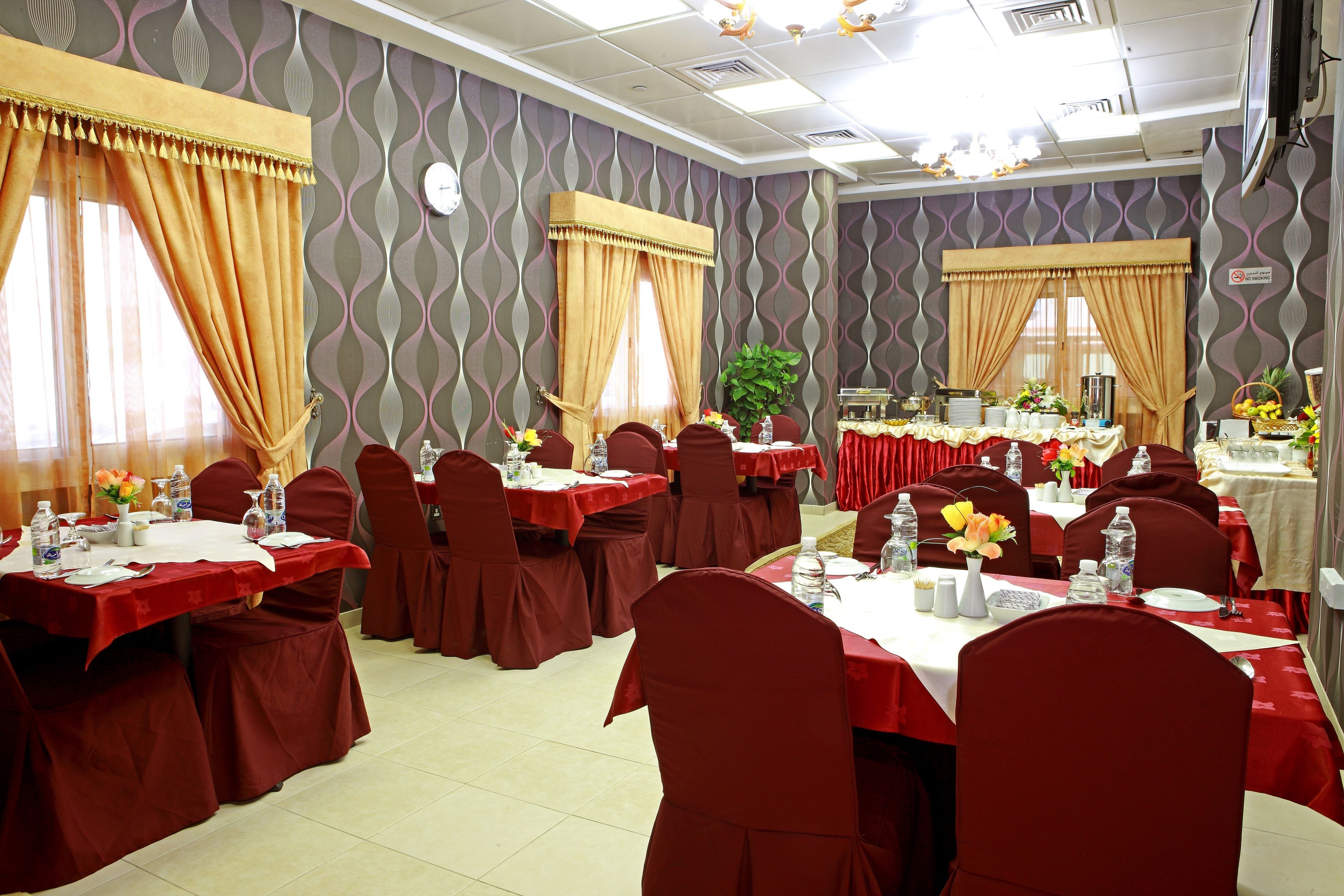 A banquet hall with multiple tables set for dining, each with red tablecloths and matching chairs.