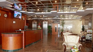 A hotel lobby with a reception desk, a television, a clock, a flower arrangement, and a seating area. - Rose Garden Hotel Apartments - Bur Dubai (Dubai)