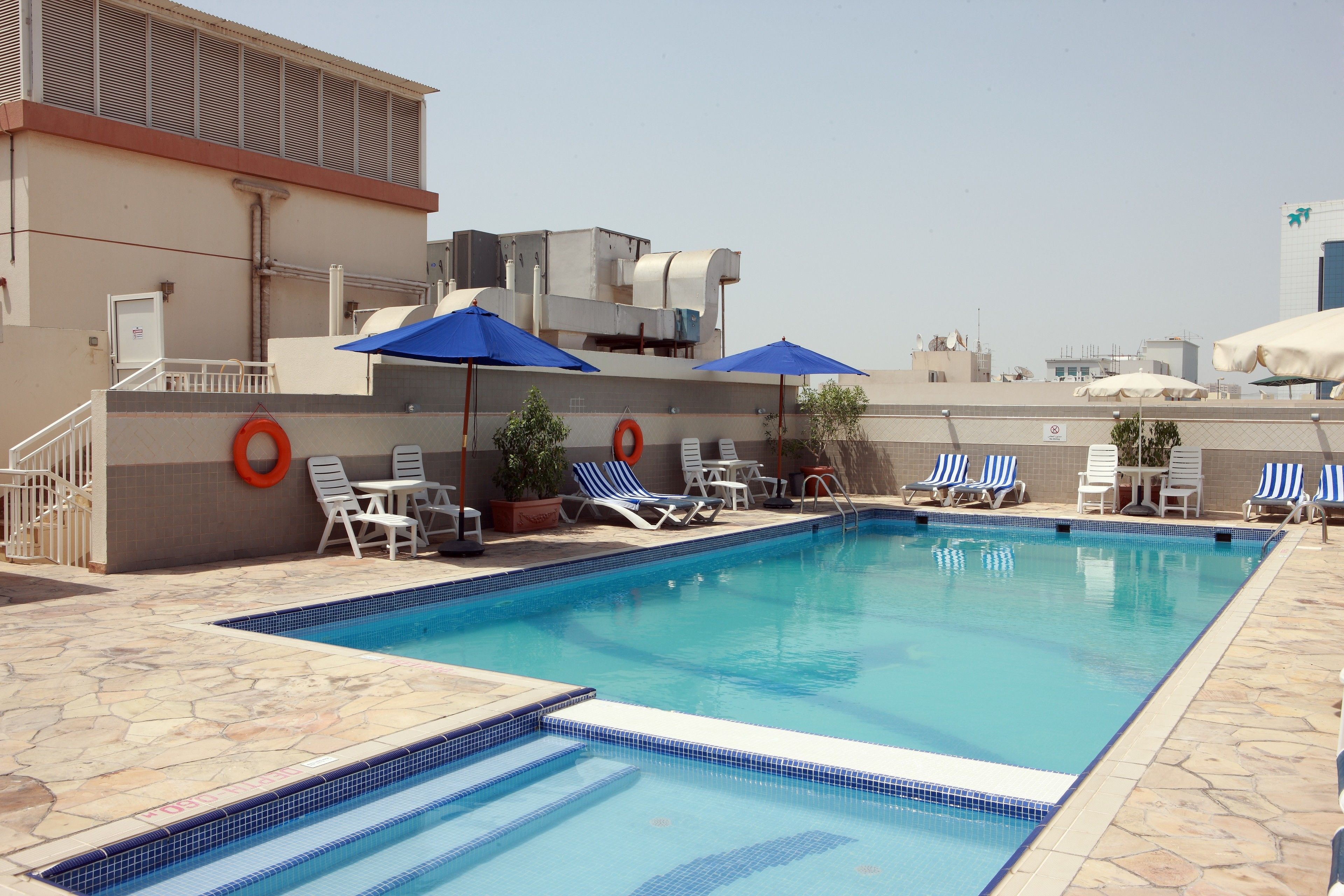 Piscina no terraço com bordas azuis em azulejo, cadeiras de descanso e guarda-sóis.