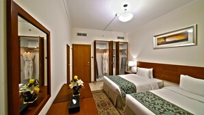 A hotel room with two beds, a large mirror, a painting, and a vase with flowers. - Rose Garden Hotel Apartments - Bur Dubai (Dubai)