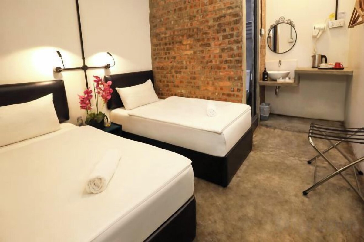 Habitación de hotel con dos camas, una pared de ladrillo, un lavabo y un espejo.