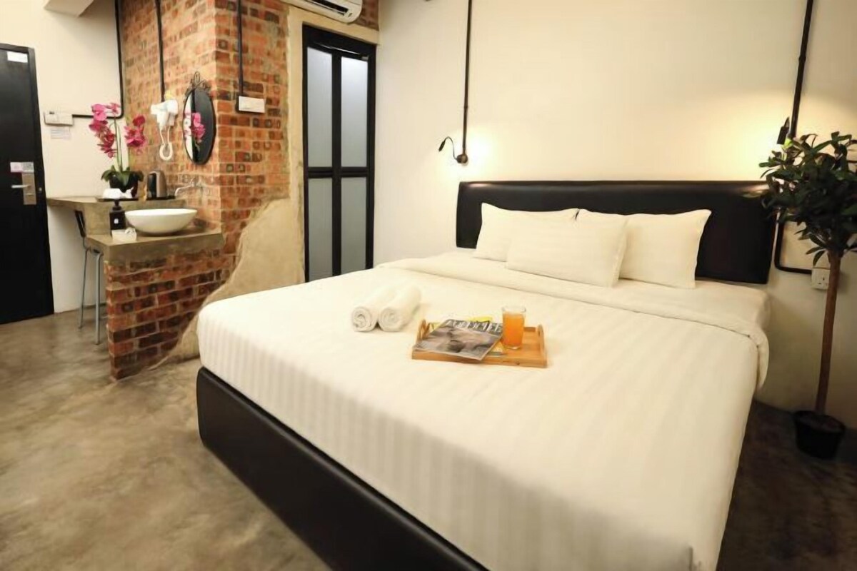 A hotel room with a brick accent wall, a bed with white bedding, a bedside table with a sink, and a mirror.