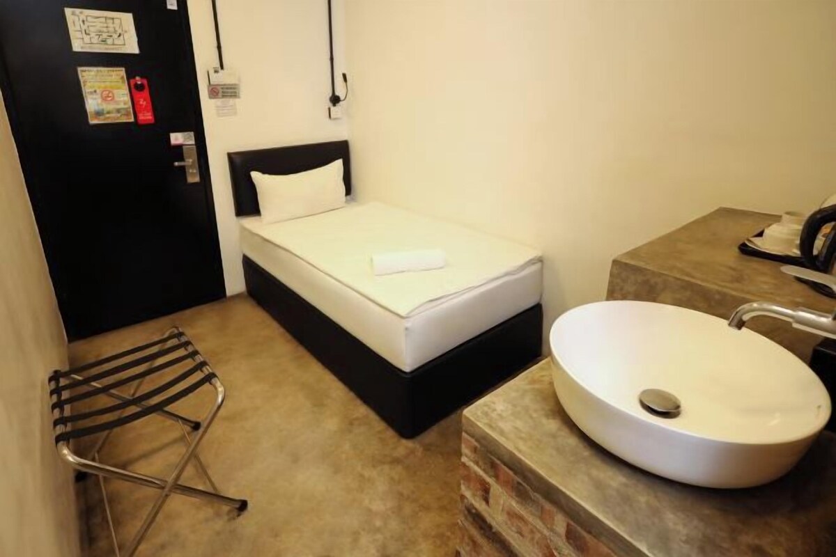 Una stanza piccola e compatta con un letto singolo, un lavandino bianco e un asciugamano sul letto.