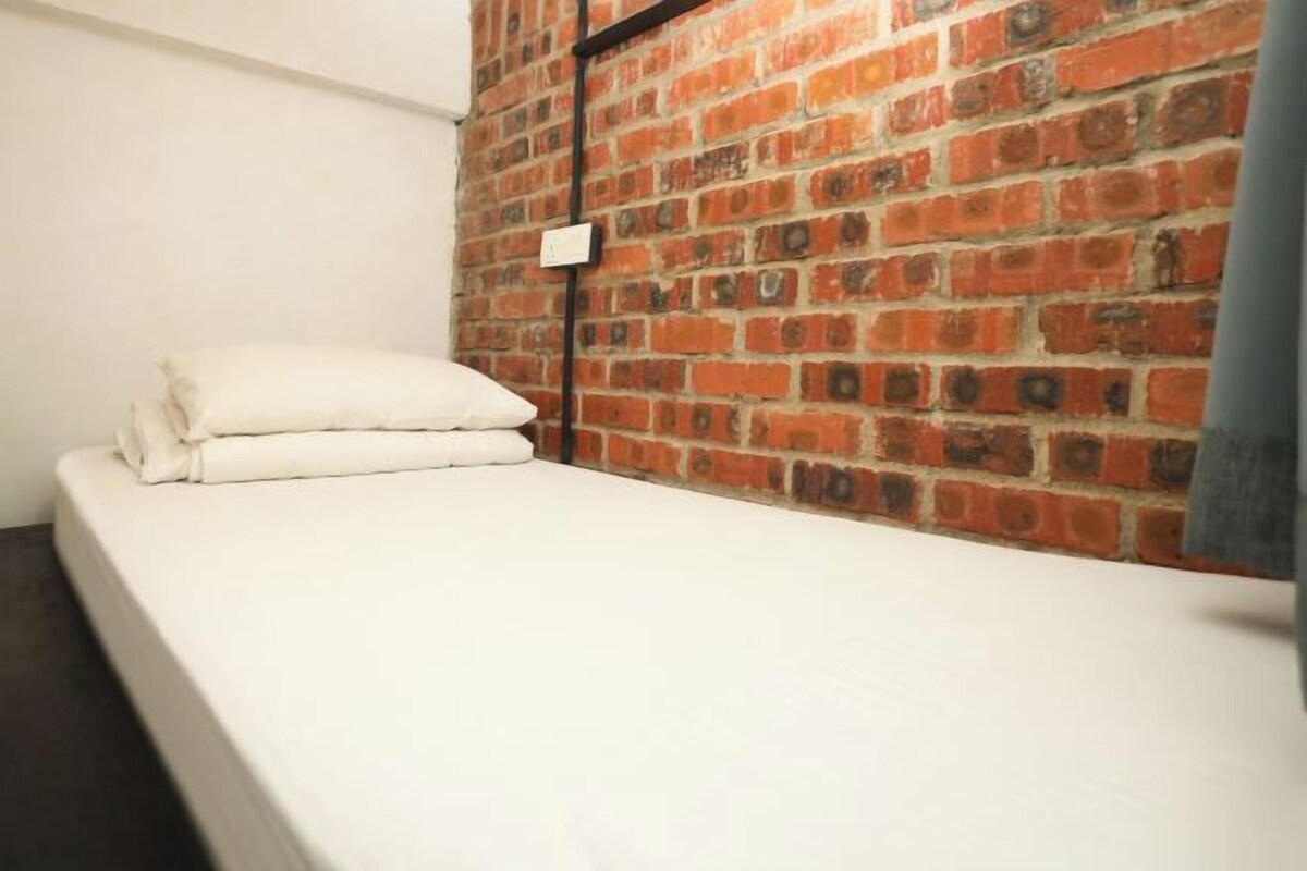 Un letto singolo con biancheria da letto bianca in una stanza con parete in mattoni.