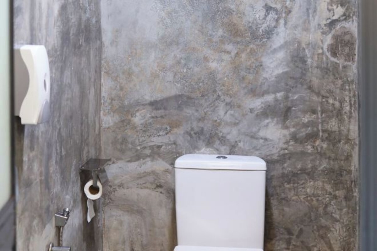 A bathroom with a stone wall, a toilet, and a paper towel dispenser.