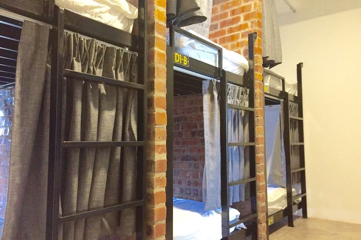 Ein Schlafsaalzimmer mit Etagenbetten, einer Backsteinwand und einem Fenster mit Vorhängen.
