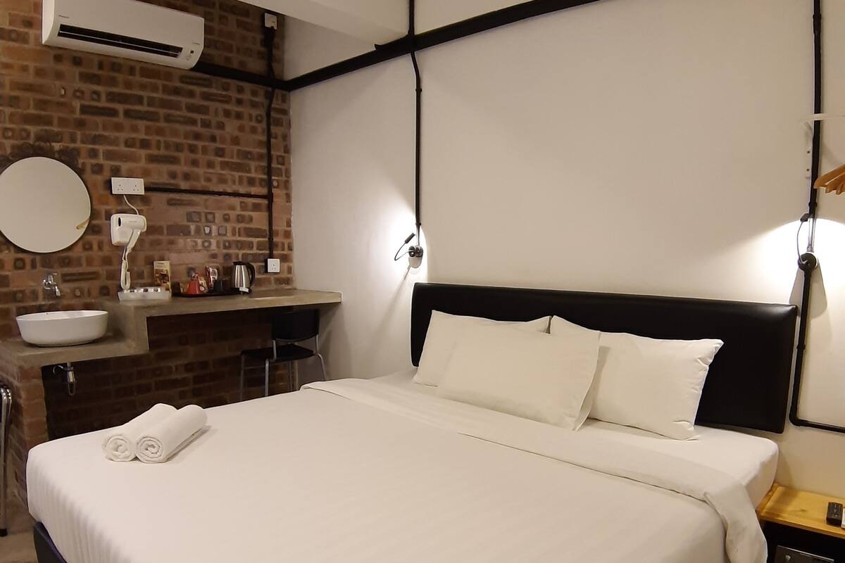 Ein Hotelzimmer mit einem großen Bett, einem runden Spiegel, einem Waschbecken und einem kleinen Tisch mit einer Lampe.