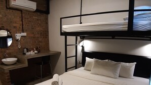 Ein Etagenbett mit weißer Matratze, ein kleiner Nachttisch und ein Spiegel. Ein Waschbecken mit Spiegel, ein Handtuch und ein Mülleimer sind ebenfalls vorhanden.