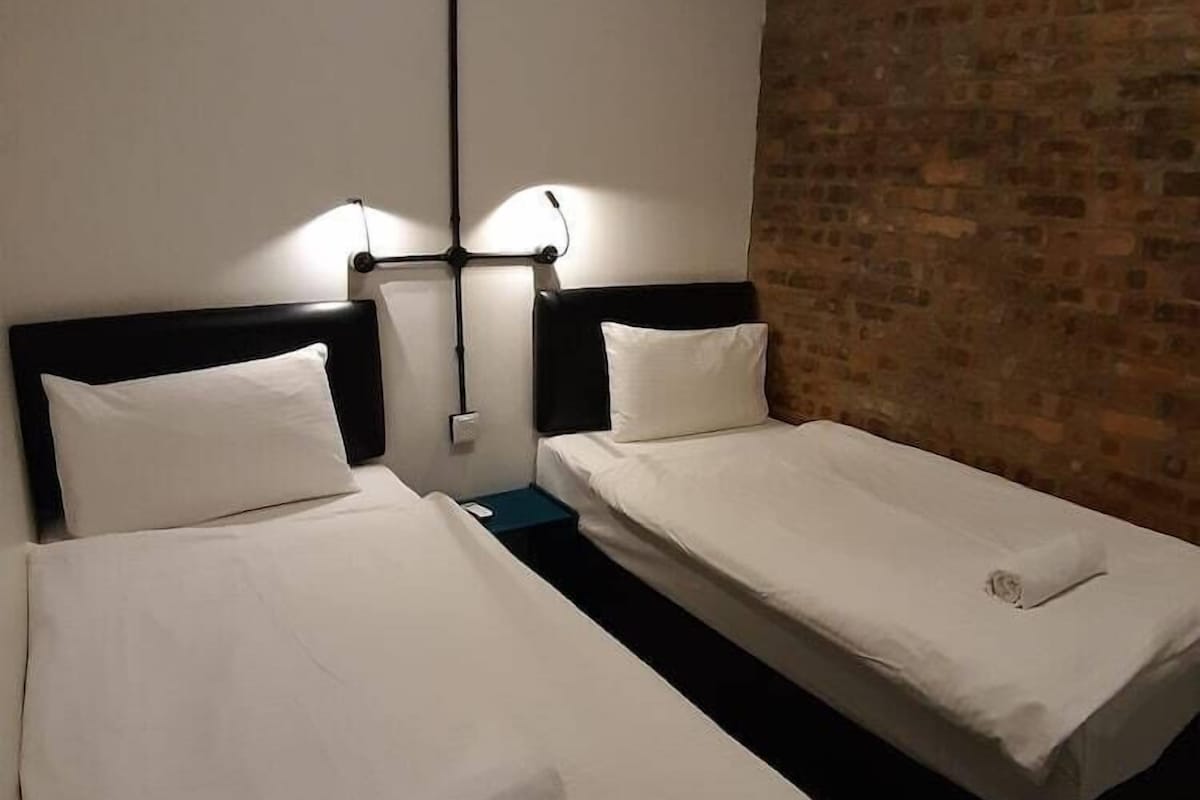 A hotel room with two single beds, a brick wall, and an air conditioning unit.