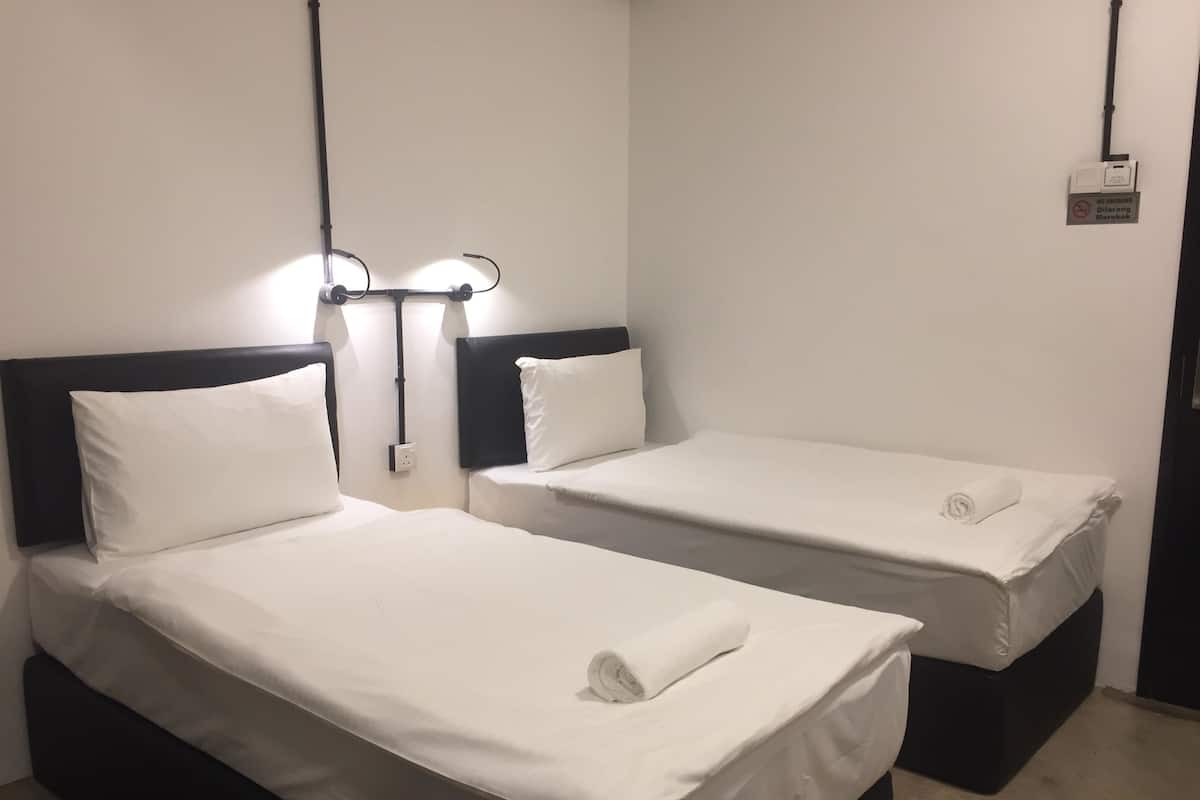 Zwei Einzelbetten mit weißen Laken und schwarzen Kopfteilen in einem Zimmer mit schlichter weißer Wand und einem Rauchverbot-Schild.