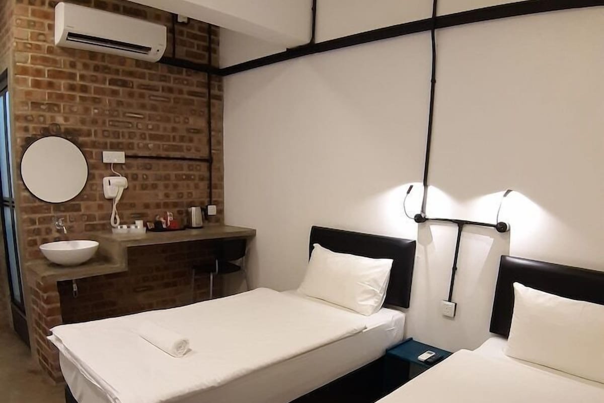 A hotel room with two beds, a brick wall, a sink, and an air conditioning unit.