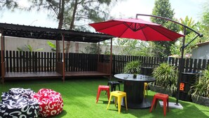 Ein Garten mit Kunstgrasanlage, einem runden Tisch, roten und gelben Hocker und einem roten Sonnenschirm.