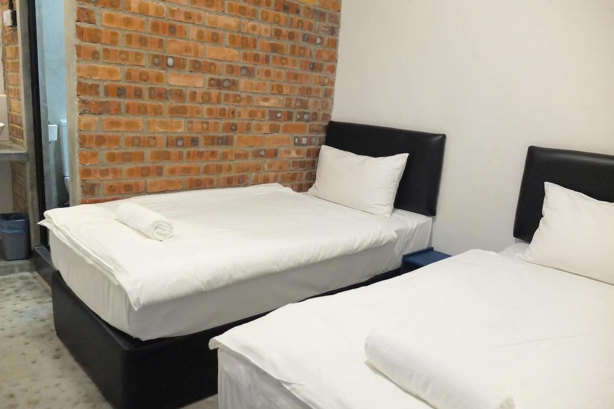 Zwei Betten mit weißen Laken in einem Zimmer, das eine Ziegelwand und ein schwarzes Kopfteil zeigt.