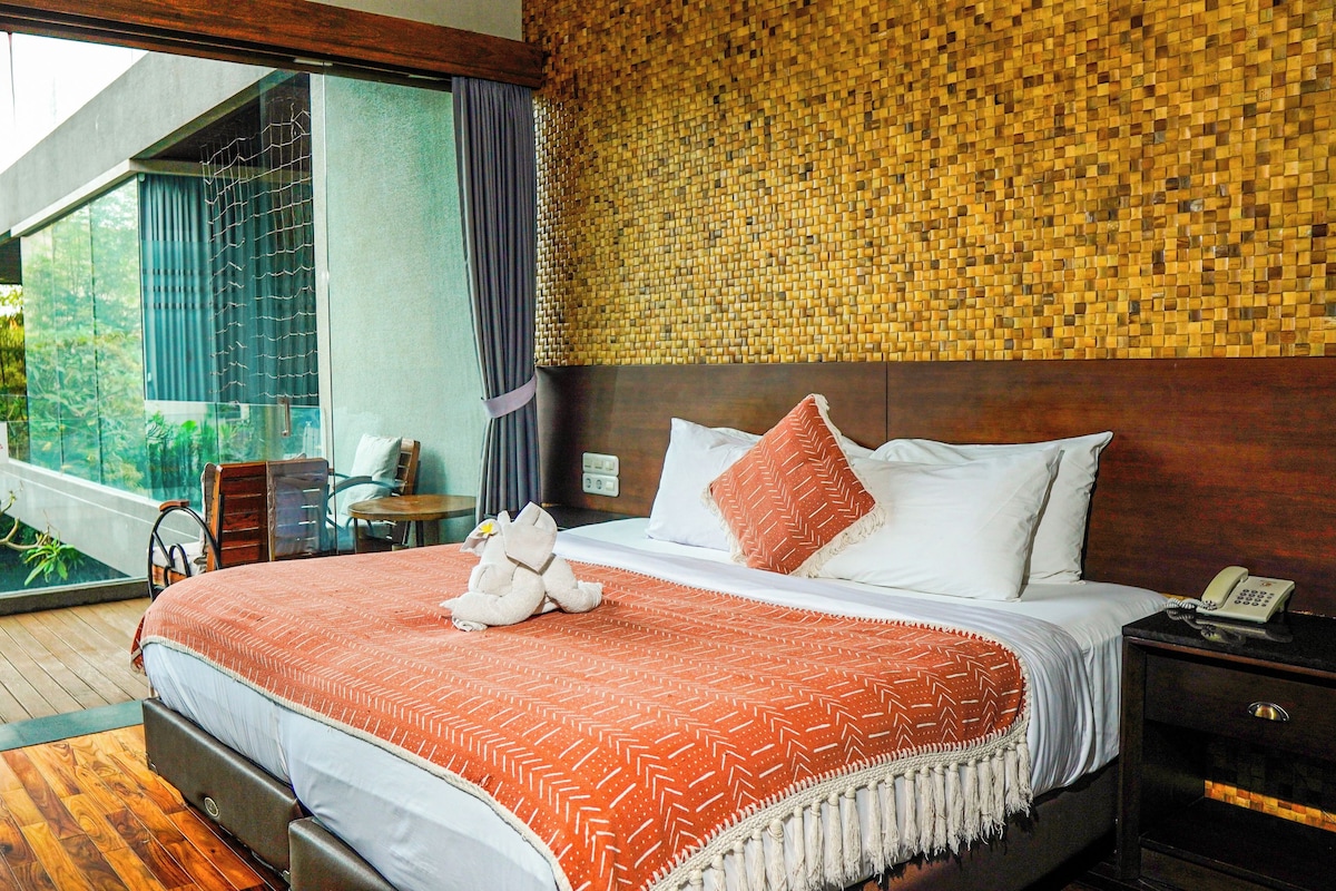 Habitación de hotel moderna con una cama grande, piso de madera, vista a espacios verdes y una pared de tejido.