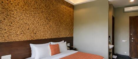A hotel room with a large bed, wooden flooring, a textured wall, and a modern ceiling design.