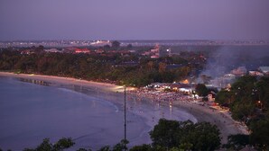 Una playa con gente, un faro y un aeropuerto a lo lejos.