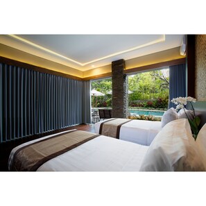 Quarto de hotel com duas camas, um pilar de pedra, vista para uma piscina e área de jantar com guarda-sóis.