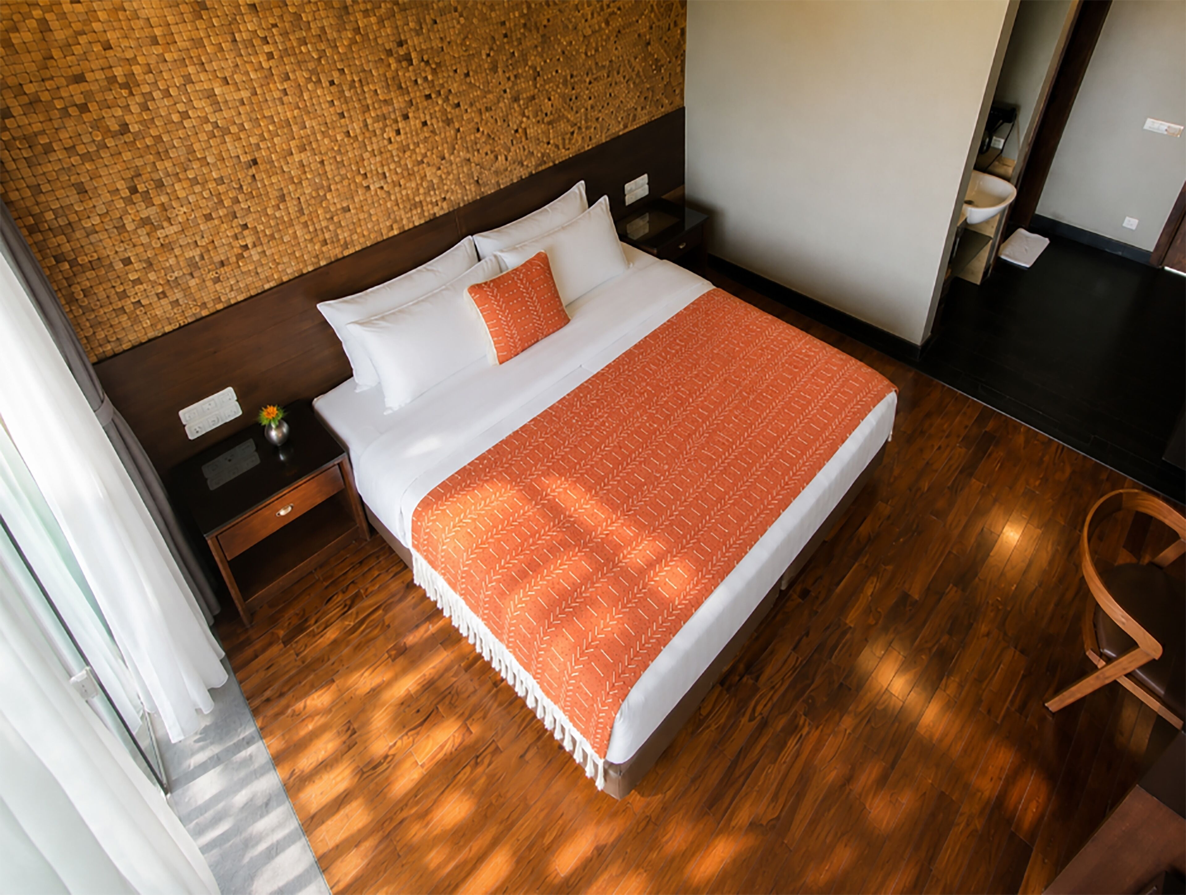 Een hotelkamer met een houten vloer, een bed met wit en oranje beddengoed, een nachtkastje en een muur met een structuur.