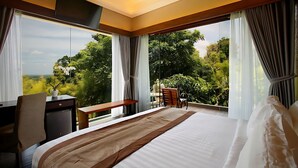 Habitación de hotel con una cama grande, un escritorio, una silla y vistas a exuberante vegetación.