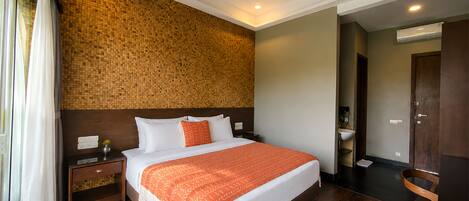 Een hotelkamer met een groot bed, houten vloeren, een wand met een structuur en een houten hoofdbord, plus een klein nachtkastje met een lamp.