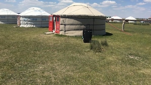 A yurt with a red door, surrounded by a grassy field and other yurts in the background. - Xanadu yurts (Xilin Gol)
