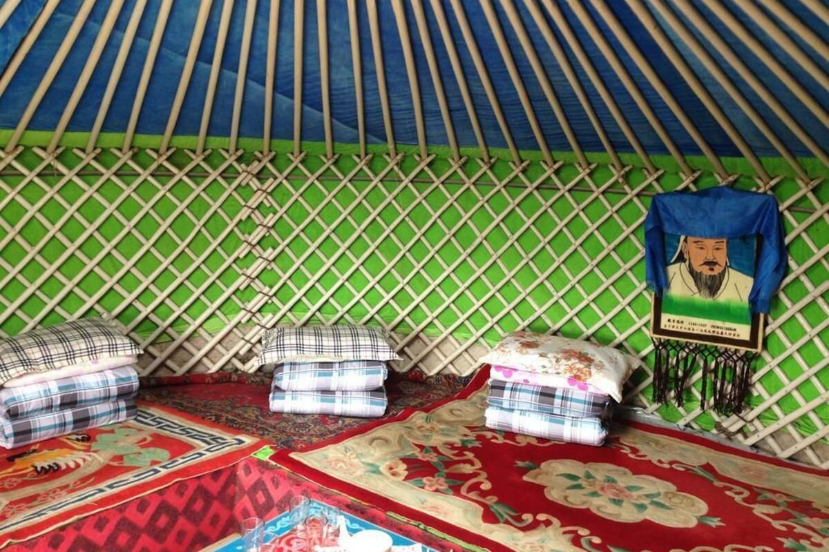 A traditional yurt with a green lattice wall, three beds with plaid bedding, and a hanging tapestry.
