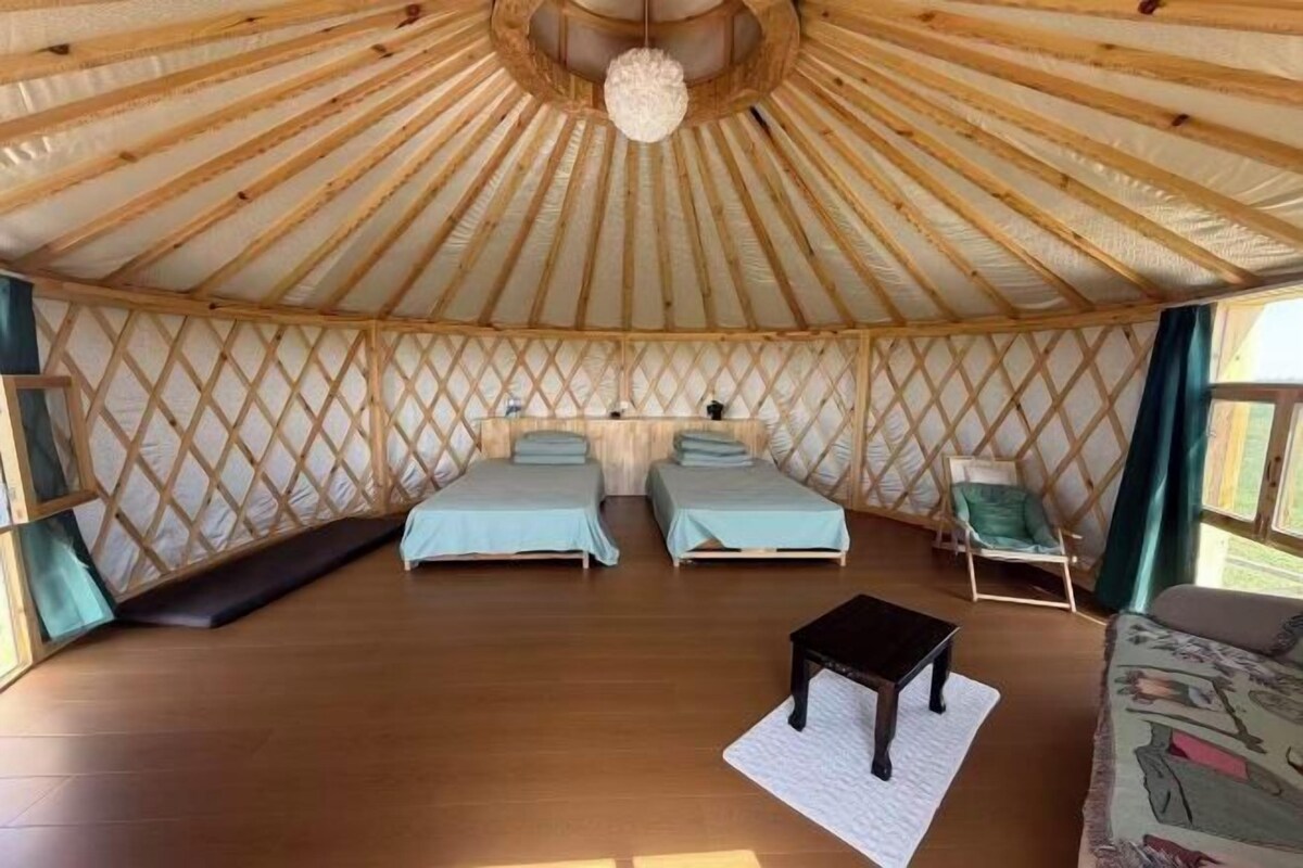 A yurt with two beds, a small table, and a chair.