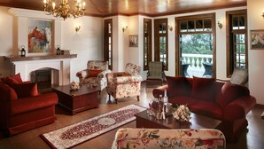 A cozy living room with a fireplace, floral armchairs, a red sofa, and a chandelier.