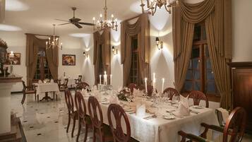 Un comedor formal con una larga mesa dispuesta para una comida, rodeada de sillas de madera con cojines verdes.