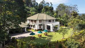 A large white building with a green roof, surrounded by lush greenery and trees.