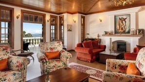 A spacious living room with floral-patterned sofas, a fireplace, and a large window offering a view of the outdoors.