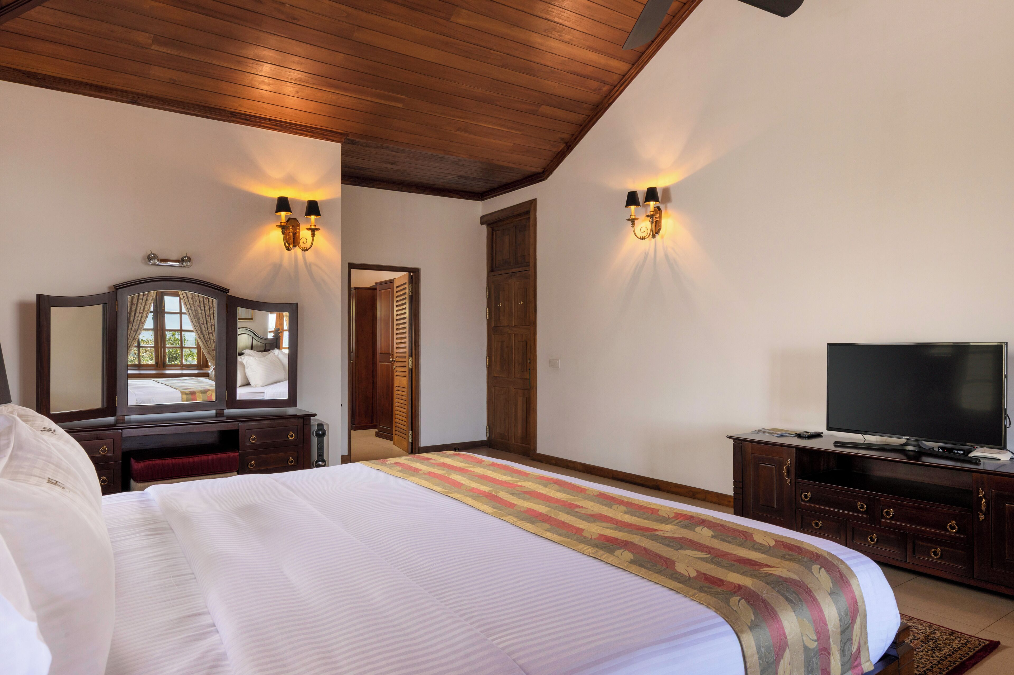 A hotel room with a large bed, a wooden ceiling, a television, and a wardrobe.