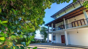 A two-story building with a balcony, surrounded by lush greenery.