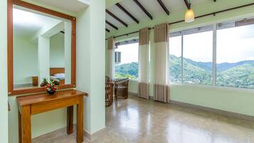 Una habitación amplia con un gran ventanal que ofrece vistas a colinas verdes, una mesa de madera con un florero y un espejo en la pared.