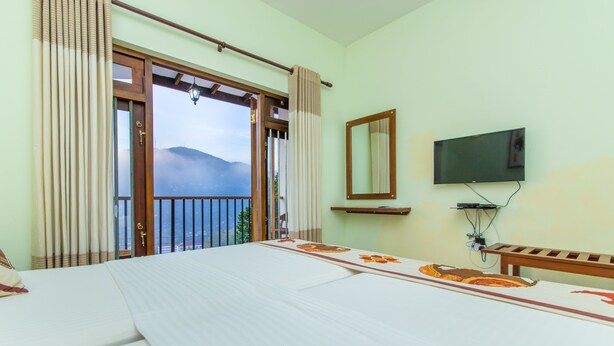Habitación de hotel con cama, televisor, ventana con cortinas y vistas a montañas.