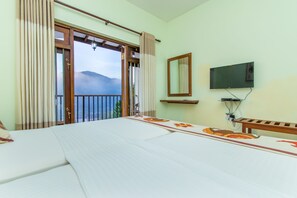 A hotel room with a bed, a TV, a window with curtains, and a view of mountains. - Jack Tree Lodge (Kandy)