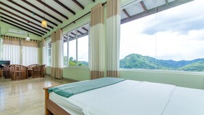 Una habitación con una cama, sillas de madera, una mesa y un ventanal con vistas a colinas verdes.